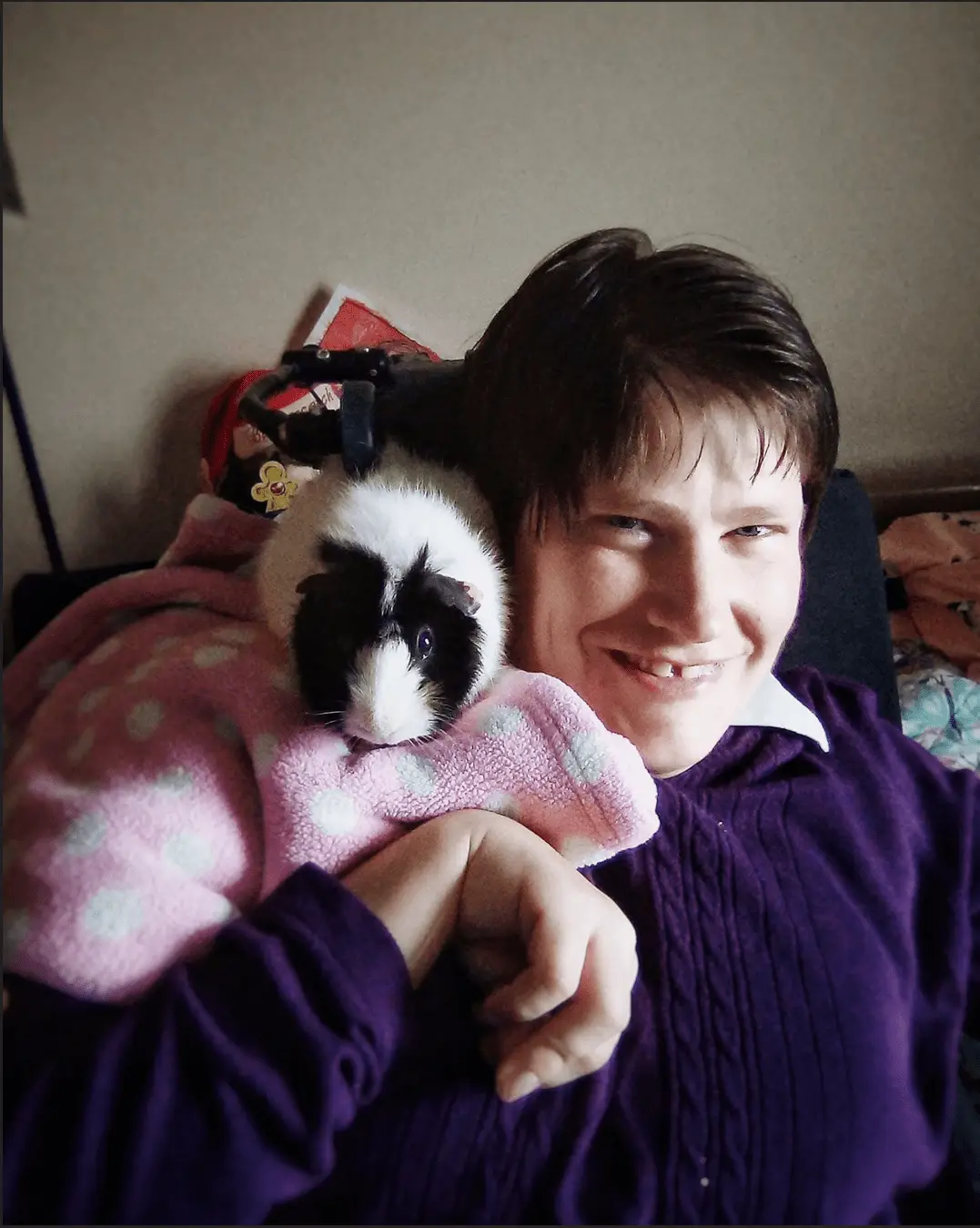 Heather, founder of The Healing Project, smiling and holding a guinea pig wrapped in a pink blanket